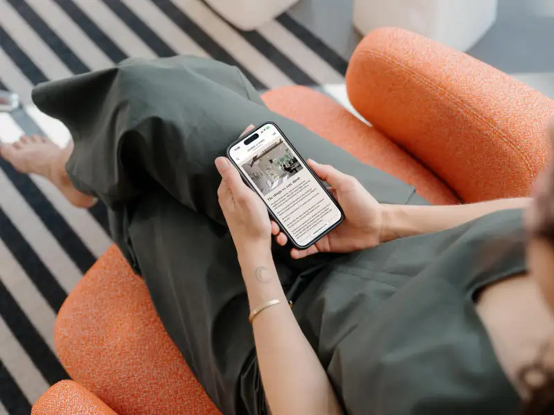 mockuuups iphone 15 pro mockup in a womans hand on a cozy couch